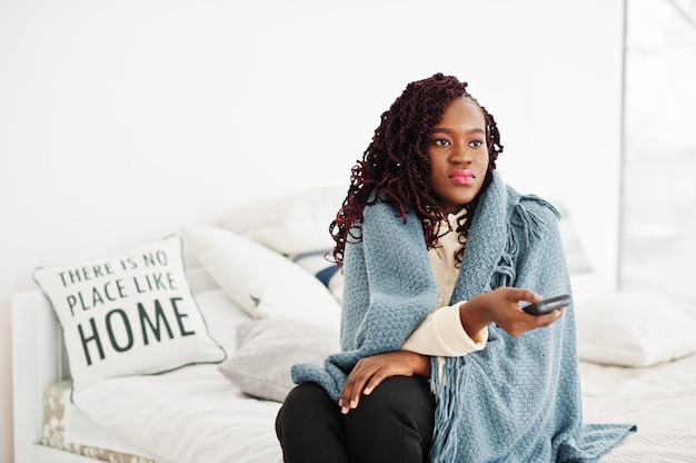 Mulher africana assistindo tv em casa e segurando um controle remoto na cama