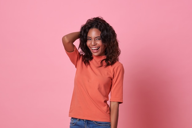 Mulher africana bonita sorridente feliz olhando para a câmera, vestindo camiseta laranja casual, isolada no fundo rosa.