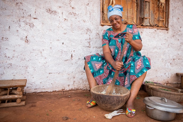 Mulher africana cozinha usando um almofariz e pilão ela está vestida com um vestido tradicional e ela está na aldeia