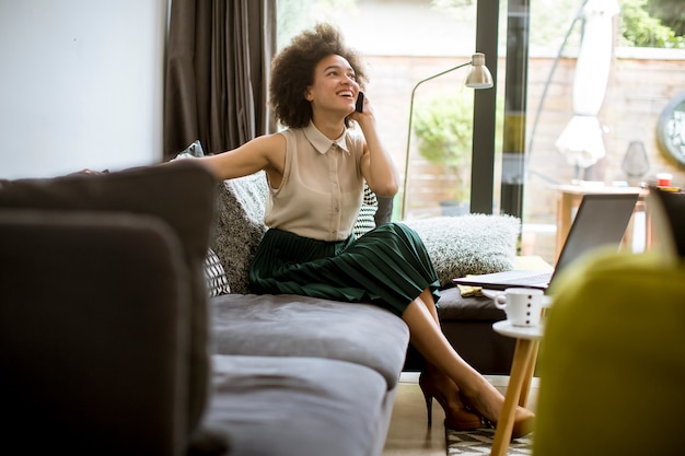 Foto mulher africana de cabelo encaracolado jovem relaxando em casa e usando telefone celular