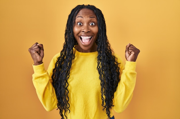 Mulher africana em pé sobre fundo amarelo comemorando surpresa e surpresa pelo sucesso com os braços levantados e olhos abertos. conceito de vencedor.