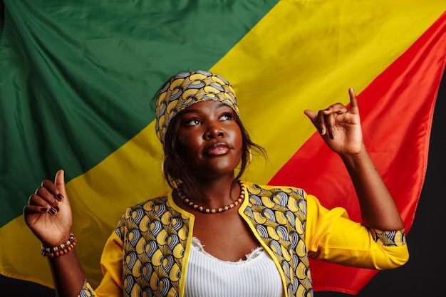 Mulher africana em roupas nacionais posando e dançando com polegares para cima contra a bandeira da república do congo