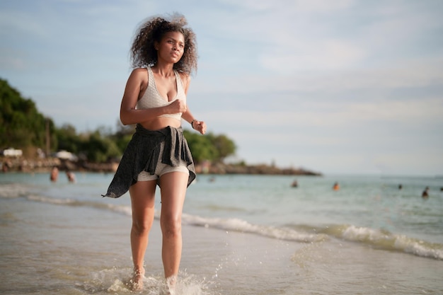 Mulher africana em sutiã esportivo está correndo na praia para treino ao ar livre Retrato sexy senhora africana asiática se preparando para fitness na praia