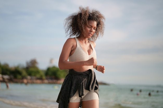 Mulher africana em sutiã esportivo está correndo na praia para treino ao ar livre Retrato sexy senhora africana asiática se preparando para fitness na praia