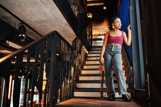 Mulher africana em top marsala vermelho e jeans posou no interior