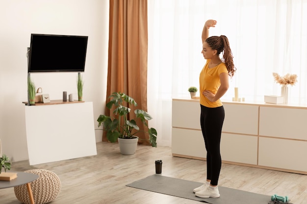 Mulher africana esticando as mãos durante o treino assistindo tv em casa