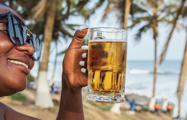 Foto mulher africana feliz bebendo uma cerveja em um bar de praia em accra, gana