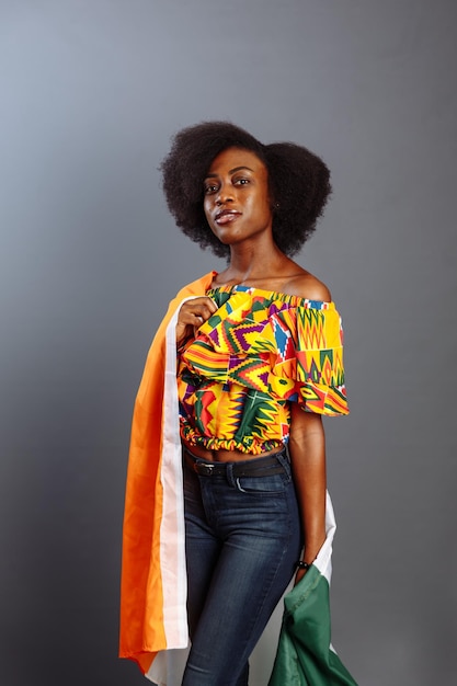 Mulher africana feliz em roupas nacionais sorrindo e posando com uma bandeira Costa do Marfim C te d'Ivoire isolada sobre um fundo cinza