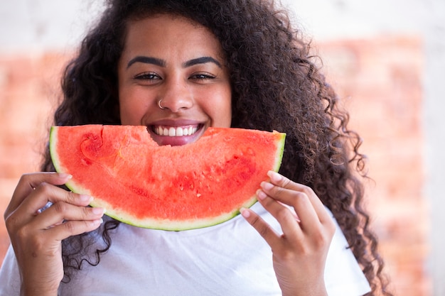 Mulher africana feliz na cozinha segurando uma fatia de melancia