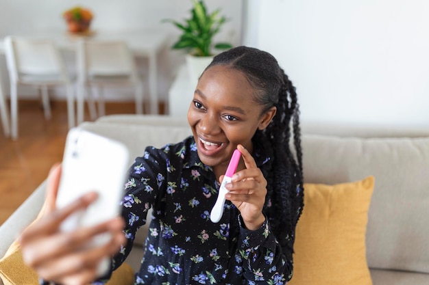 Mulher africana grávida feliz está mostrando seu teste de gravidez e tirando selfie fazendo videochamada Mulher feliz tirando foto do teste de gravidez com telefone celular e postando foto nas mídias sociais