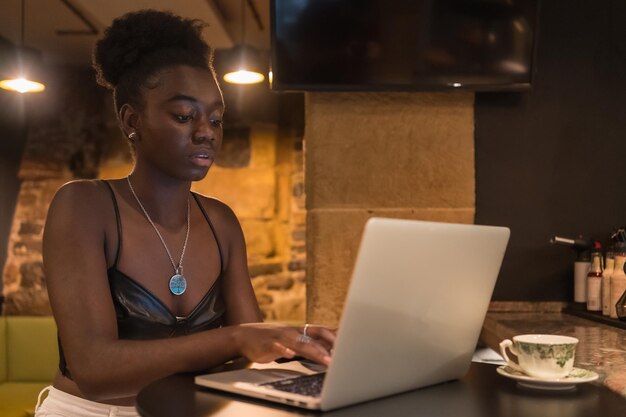 Mulher africana jovem concentrada usando laptop em uma cafeteria