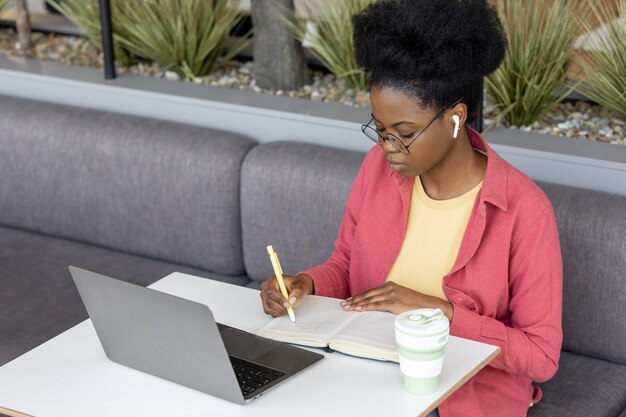 Mulher africana jovem e bonita em uma camisa rosa em uma sala de coworking trabalhando em um laptop