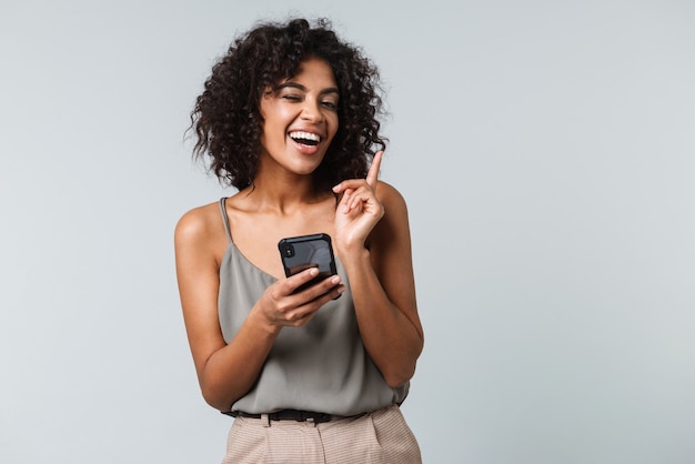 Mulher africana jovem e feliz, vestida de maneira casual, isolada, usando telefone celular