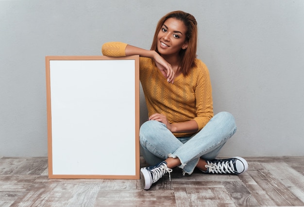 Mulher africana muito sorridente, de suéter e jeans, sentada no chão de madeira