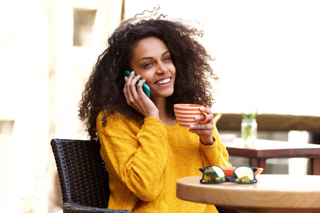 Mulher africana nova de sorriso que fala no telemóvel no café