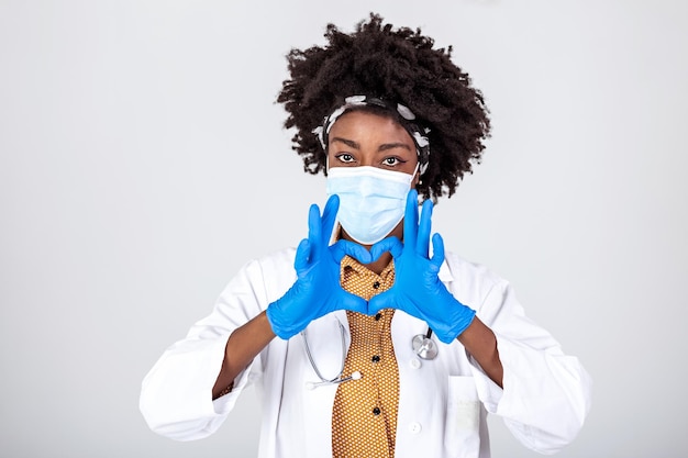 Mulher africana profissional médico enfermeiro médico usar máscara de rosto luvas uniforme mostrando coração mãos forma amor médico cuidados e segurança símbolo coronavirus sinal de proteção de saúde conceito Closeup