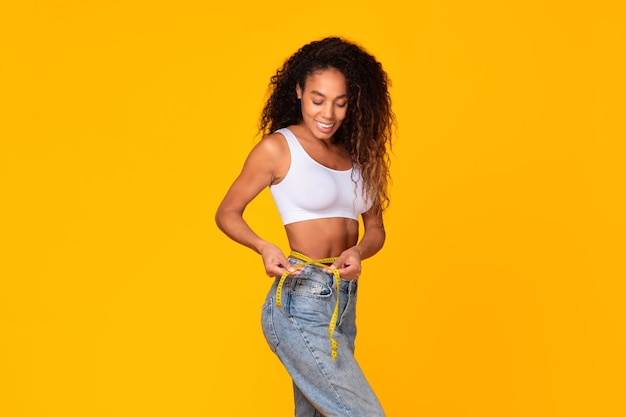 Foto mulher africana segurando fita métrica em torno da cintura com fundo amarelo