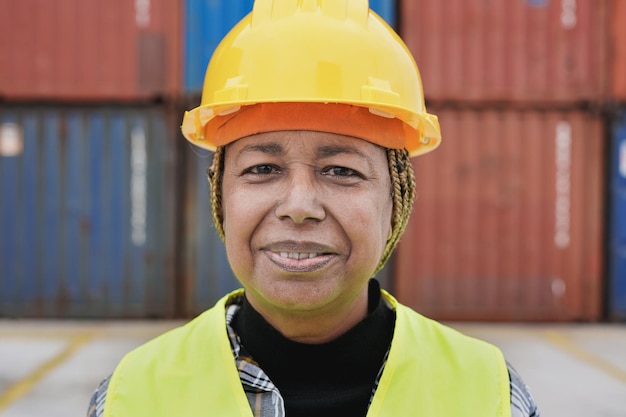 Mulher africana sênior trabalhando no porto enquanto usava capacete de segurança e colete de segurança Porto de contêineres de importação e exportação em segundo plano