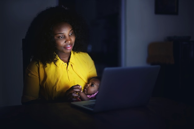 Mulher africana sentada à noite com o bebê na frente do laptop