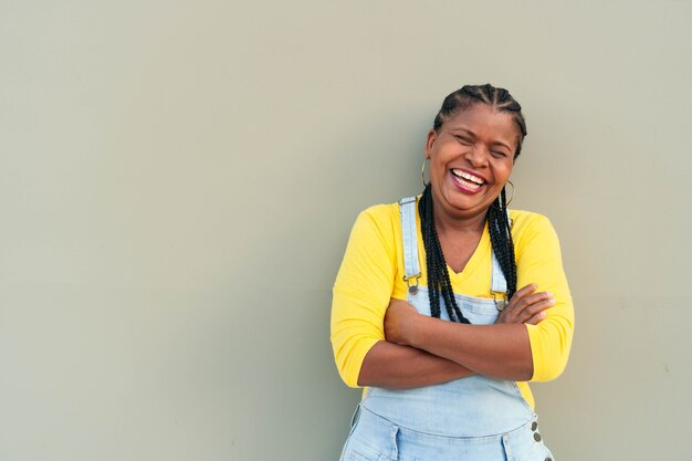 Mulher africana sorridente encostada em uma parede cinza