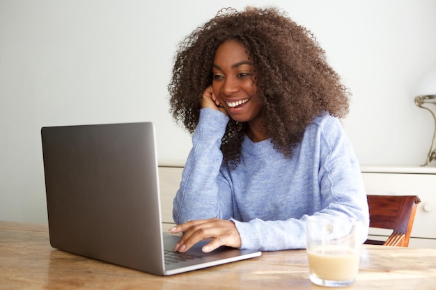 Mulher africana sorridente sentada em casa e trabalhando no laptop