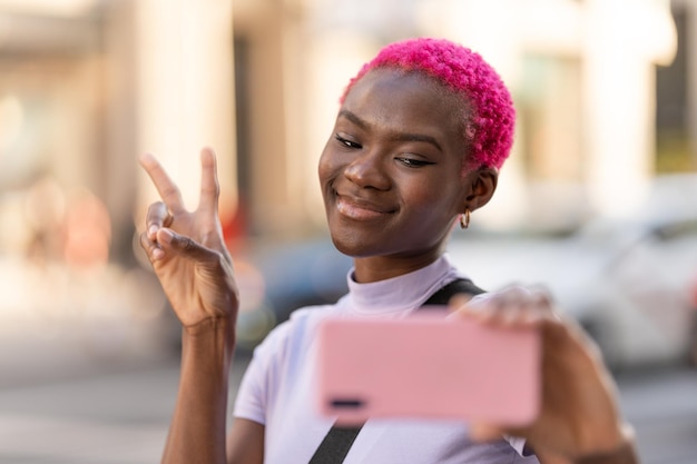 Mulher africana sorridente tomando selfie enquanto gesticula vitória ao ar livre