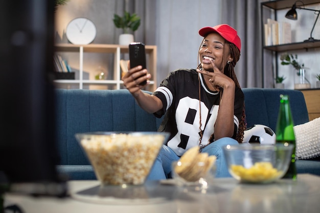 Mulher africana tirando selfie em smartphone durante jogo de futebol