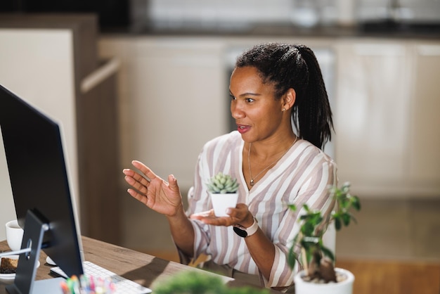 Foto mulher africana vlogando sobre cuidados com as plantas e mostrando a suculenta de sua casa enquanto se reunia on-line em seu computador em casa.