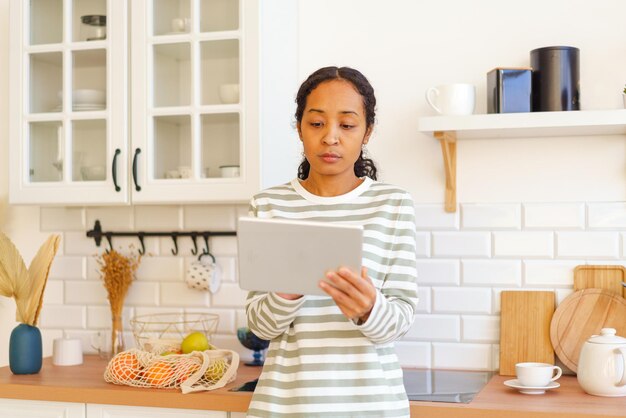 Mulher afro-americana à procura de receita no tablet antes de cozinhar uma refeição na cozinha