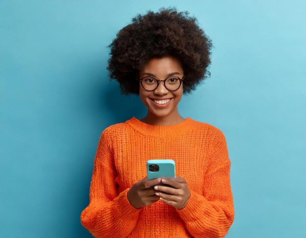 mulher afro-americana alegre e encantada enviando mensagens de texto em um aparelho de telefone celular moderno com costas azuis