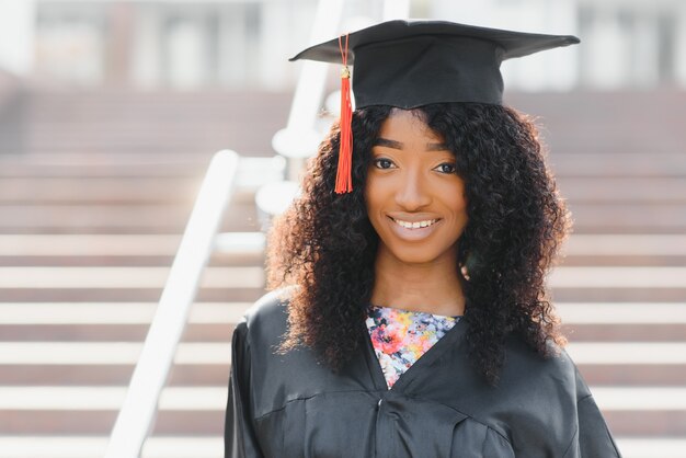 Mulher afro-americana alegre graduada em frente ao prédio da universidade