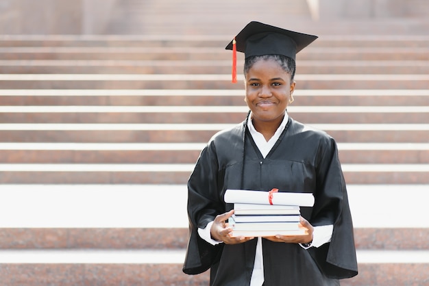 Mulher afro-americana alegre graduada em frente ao prédio da universidade