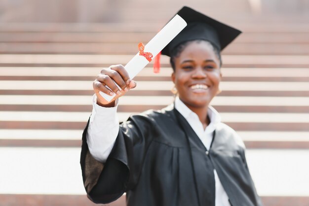 Mulher afro-americana alegre graduada em frente ao prédio da universidade