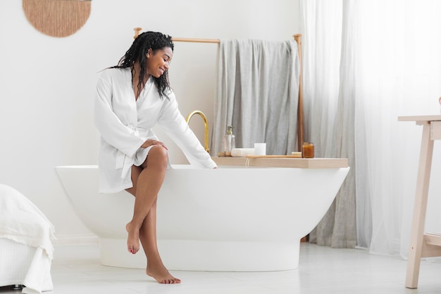 Mulher afro-americana atraente sorridente sentada na banheira e tocando água