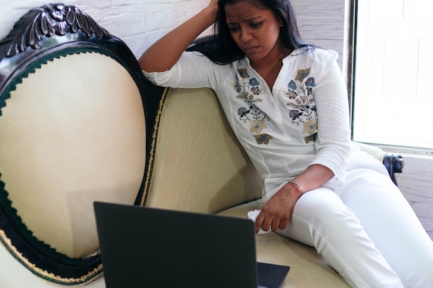 Foto mulher afro-americana chorando e colocando a cabeça na mão enquanto olha para a tela do laptop para o psicólogo.