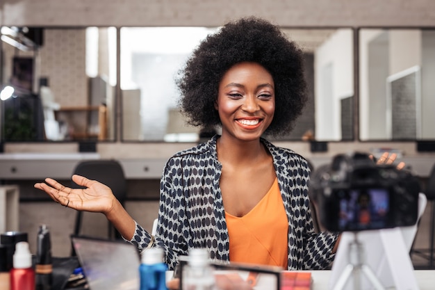 Mulher afro-americana com cabelo encaracolado com aparência positiva durante a gravação de vídeo