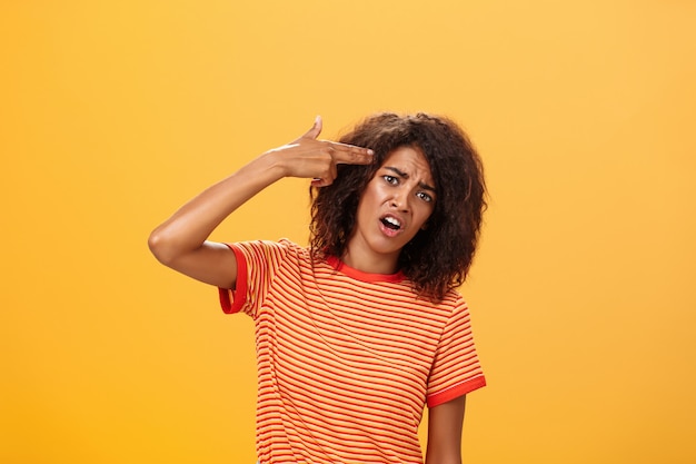 Mulher afro-americana com camiseta listrada inclinando a cabeça, colocando o dedo da arma na testa, cometendo suicídio