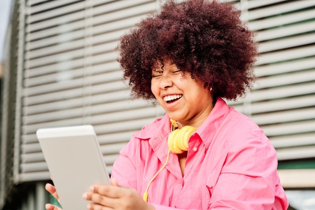 Mulher afro-americana com estilo de cabelo encaracolado fazendo uma chamada de vídeo com seu tablet pc jovem rindo enquanto usa redes sociais