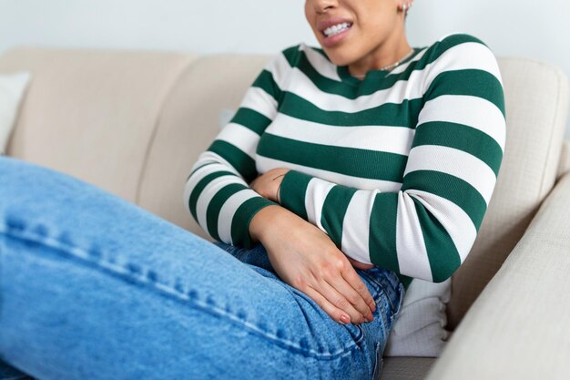 Foto mulher afro-americana com expressão dolorosa segurando as mãos contra a barriga sofrendo dor do período menstrual deitada triste na cama de casa com cãibra na barriga no conceito de saúde feminina