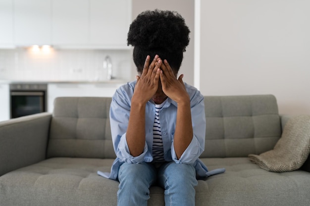 Mulher afro-americana confusa cobre o rosto com as mãos depois de brigar com amigos sentado no sofá