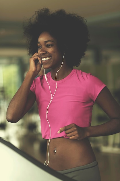 mulher afro-americana correndo em uma esteira na academia enquanto ouve música em fones de ouvido