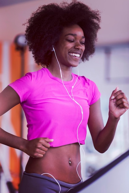 mulher afro-americana correndo em uma esteira na academia enquanto ouve música em fones de ouvido