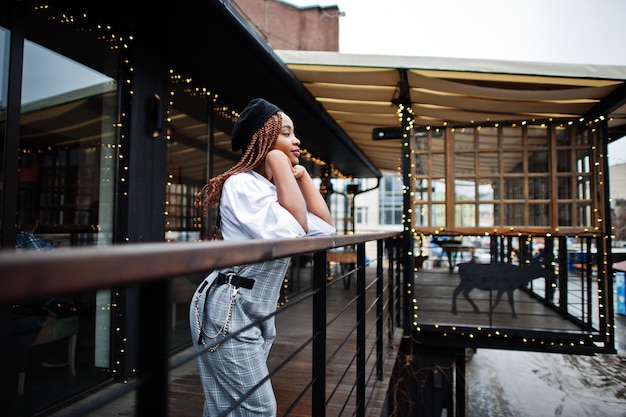 Mulher afro-americana de macacão e boina posou no terraço ao ar livre com guirlanda de decorações de natal