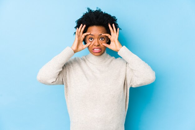 Mulher afro-americana de meia idade contra um azul isolado, mantendo os olhos abertos para encontrar uma oportunidade de sucesso.