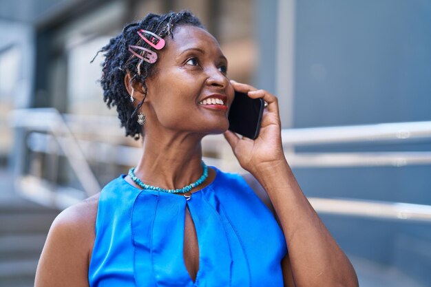 Mulher afro-americana de meia-idade sorrindo confiante falando no smartphone na rua