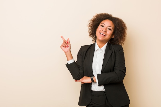 Mulher afro-americana de negócios jovem sorrindo alegremente, apontando com o dedo indicador afastado.