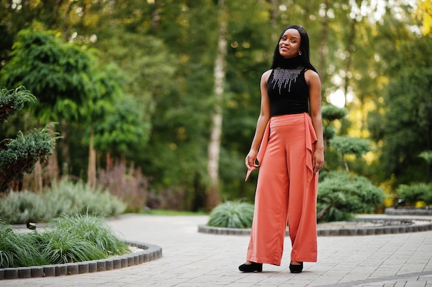 Mulher afro-americana elegante em calças de pêssego e blusa preta posam ao ar livre.