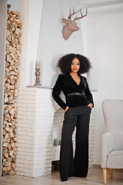 Mulher afro-americana elegante em preto posou no quarto contra a lareira