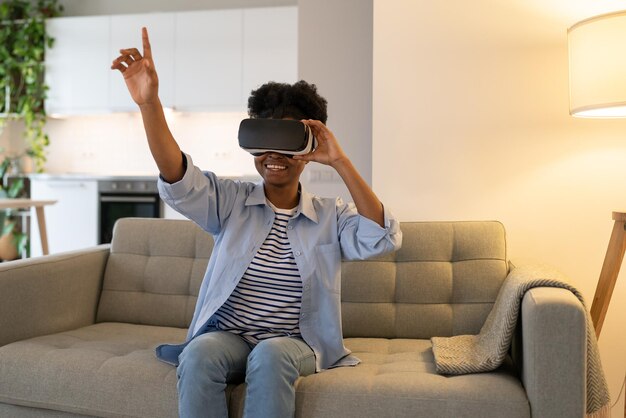 Mulher afro-americana encorajada usando óculos de realidade virtual para assistir filmes em 3d sentada no sofá