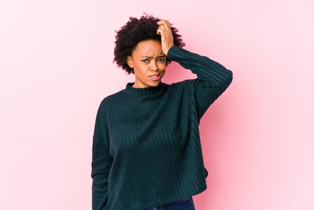 Mulher afro-americana envelhecida média contra uma parede rosa isolada sendo chocada, lembrou-se de uma reunião importante.